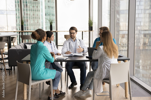 Diverse doctors take part in team meeting gather in clinic conference room, participate in collaborative discussion to review patient case, treatment option, strategize about further medical procedure