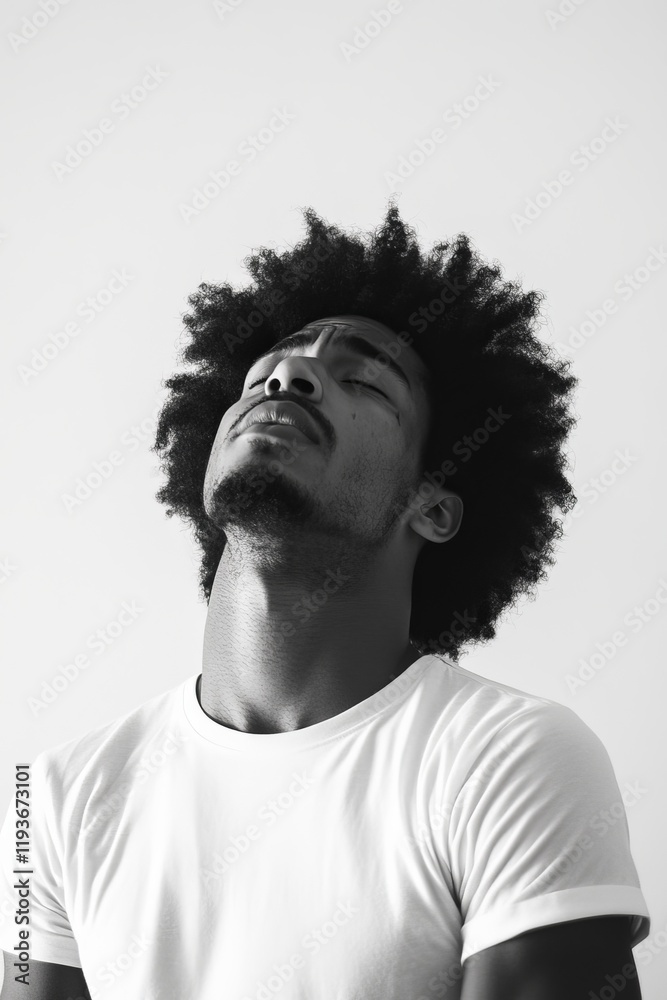 Obraz premium Black and white portrait of a man in a white t-shirt with an expressive, introspective pose looking upwards.