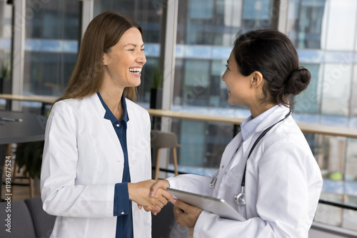 Women colleagues, hospital staff members having friendly informal talk standing in clinic office, greeting, shake hands, express respect, finish medical concilium meeting successfully, reach agreement
