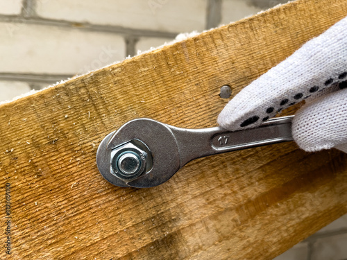 Fotografija A detailed shot of a hand tightening a bolt on a wooden beam using a wrench