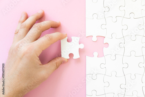 Hand holding last white piece of jigsaw puzzle, top view