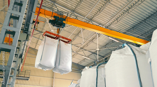 Industrial Crane Lifting Bulk Bags in Warehouse. Close-up of an industrial crane lifting large white bulk bags inside a warehouse
