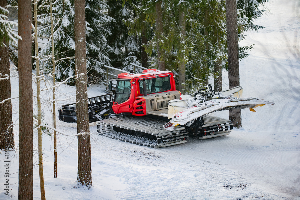 Large red snow tractor for ski slope re-tracking and snow grooming on ski slope in forest Large red snow tractor for ski slope re-tracking and snow grooming on ski slope in forest