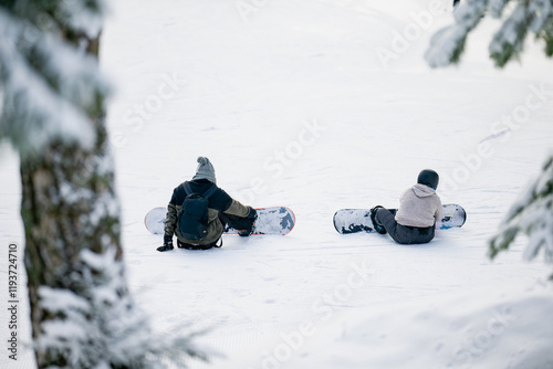 Couple of snowboarders sitting and getting ready to ride down on ski slope in alps ski resorts of deep pine forests photo