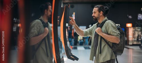 A man checks in for a plane at the electronic check-in desk. A young tourist guy at the airport gets a ticket at the check-in screen