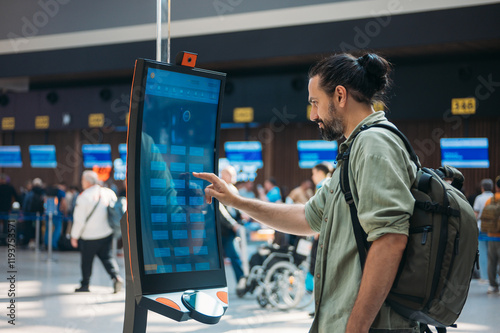 A man checks in for a plane at the electronic check-in desk. A young tourist guy at the airport gets a ticket at the check-in screen