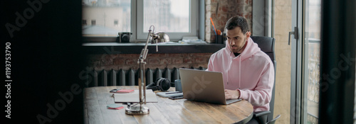 A young man works alone in the office with a laptop. Handsome guy sits at a table, works at a computer