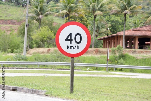 Placa de sinalização de transito na beirada de uma rodovia indicando 40 km por hora na cor vermelha e fundo desfocado.
