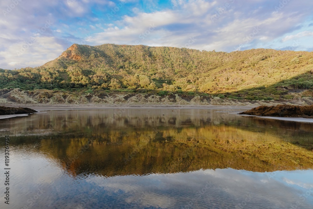 Tranquil reflection of a lush hillside on a calm coastal water. Perfect for nature lovers. Bethells Beach, Auckland, New Zealand Tranquil reflection of a lush hillside on a calm coastal water. Perfect for nature lovers. Bethells Beach, Auckland, New Zealand