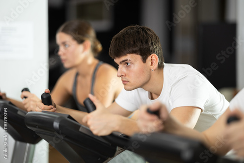Guy hardly perform track on stationary bicycle, pedaling and exercising in fitness class. Fitness equipment, athlete engaged in physical task during training, work out, participate in sport challenge