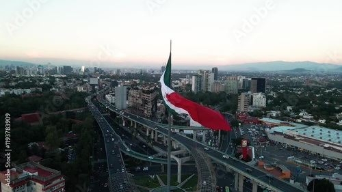 Drone footage of a huge Mexican flag waving with a view of Mexico city with buildings and traffic