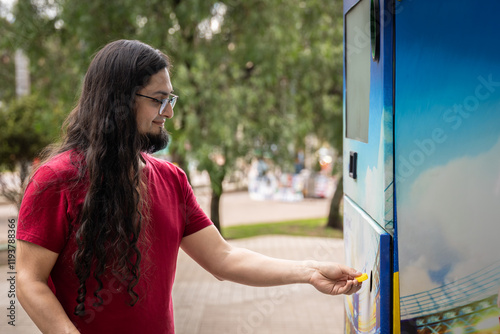 Young hispanic man using bottle deposit point. Man recycling plastic bottle via reverse vending machine. Hispanic reciclying bottles photo