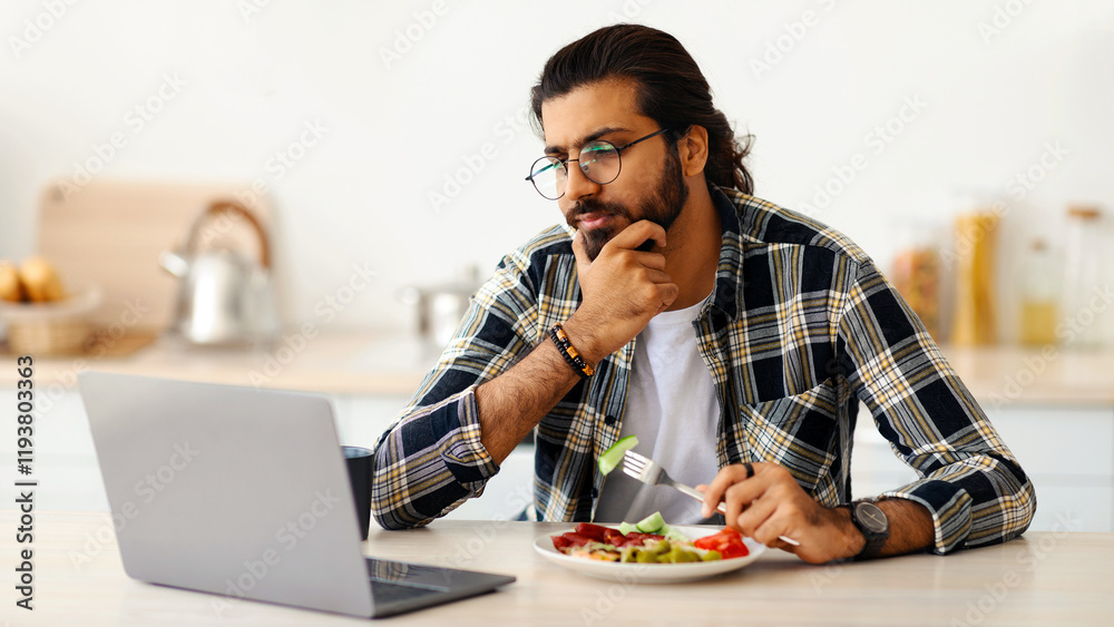 Pensive indian man freelancer having snack while working from home during coronavirus pandemic, stressed arab guy eating healthy food, looking at laptop screen, need for vacation, copy space Pensive indian man freelancer having snack while working from home during coronavirus pandemic, stressed arab guy eating healthy food, looking at laptop screen, need for vacation, copy space