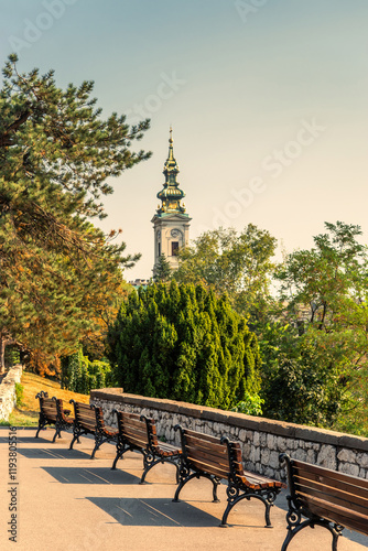 Resting place with benches on the Kalemegdan fortress wall with the Cathedral Church of Saint Michael the Archangel behind green trees photo