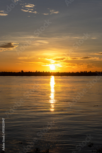 A serene sunset scene showcasing the golden sun descending over the horizon, casting a radiant reflection on the calm river. Barranquilla