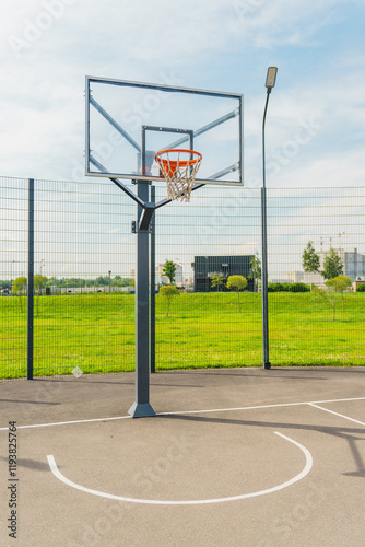 Basketball hoop on an outdoor court surrounded by a spacious green area on a sunny day photo