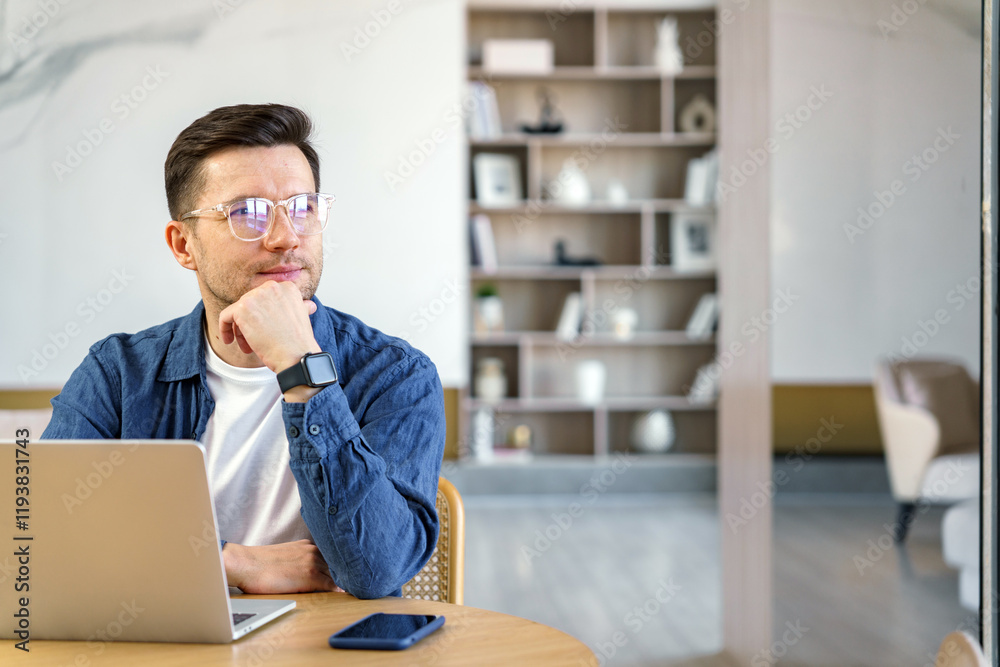 Focused young professional thinking while working on a laptop in a modern office space with minimal decor Focused young professional thinking while working on a laptop in a modern office space with minimal decor