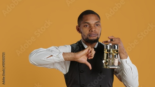 Restaurant staff giving a thumbs down sign against yellow background, carrying a cruet set with essential condiments at tables. Waiter in customer service industry, dislike symbol. Camera A. photo