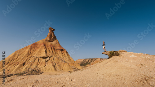 A traveler admires and photographs the magnificent Castildetierra formation in Bardenas Reales, a natural masterpiece amidst the golden hues of the arid Spanish desert.