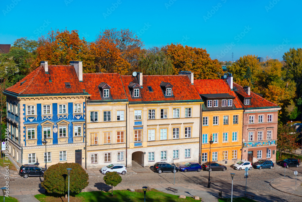 Row of charming historic houses in Warsaw, Poland, featuring colorful facades, red-tiled roofs, and dormer windows, set against a vibrant backdrop of autumn trees and a clear blue sky Row of charming historic houses in Warsaw, Poland, featuring colorful facades, red-tiled roofs, and dormer windows, set against a vibrant backdrop of autumn trees and a clear blue sky