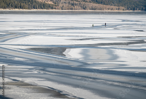 Snow patterns and two ice skaters on frozen Lake Minnewanka in Banff National Park photo