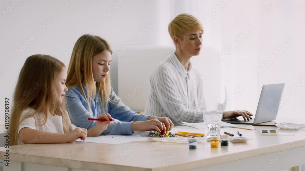 Two children are focused on drawing and crafting with colorful materials, while an adult is working on a laptop at a sunny table. The atmosphere is filled with creativity and concentration. Two children are focused on drawing and crafting with colorful materials, while an adult is working on a laptop at a sunny table. The atmosphere is filled with creativity and concentration.