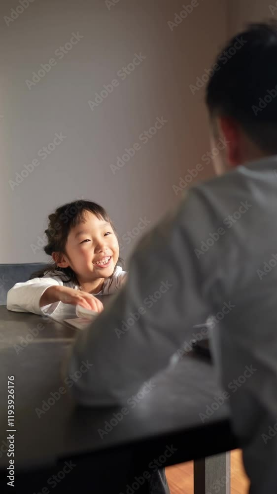 A Japanese parent and child, a woman in her 30s, a man in his 20s, and a 6-year-old girl, are studying English in the living room, wearing simple white clothes. Vertical video. A Japanese parent and child, a woman in her 30s, a man in his 20s, and a 6-year-old girl, are studying English in the living room, wearing simple white clothes. Vertical video.