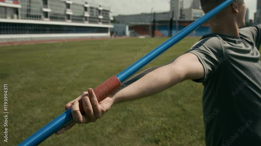 Medium rear closeup of arm of unrecognizable male track and field athlete holding javelin, aiming and angling before performing throw while working on his technique at outdoor stadium Medium rear closeup of arm of unrecognizable male track and field athlete holding javelin, aiming and angling before performing throw while working on his technique at outdoor stadium
