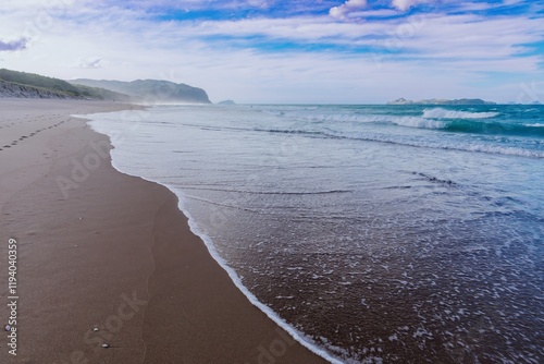 Tranquil beach scene with gentle waves lapping at the shore. Footprints in the sand lead to the ocean. Peaceful coastal view. Opoutere, Whangamata, Coromandel Peninsula, New Zealand photo