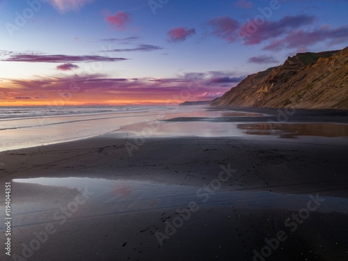 Dramatic sunset over a black sand beach. Coastal cliffs meet the ocean at twilight. Peaceful, tranquil scene. Hamiltons Gap, Awhitu, Auckland, New Zealand photo