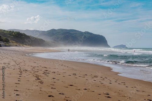 Tranquil beach scene with gentle waves, footprints in the sand, and a surfer walking along the shore. Coastal serenity. Opoutere, Whangamata, Coromandel Peninsula, New Zealand photo