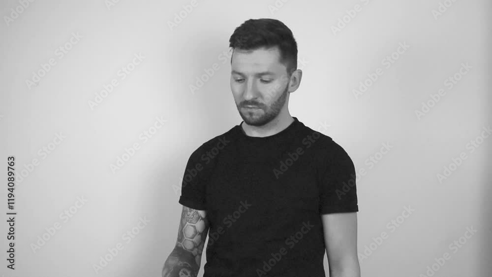 Grayscale footage of a tattooed short haired man spinning a bitcoin coin in slow motion by throwing it into the air and catching it. after catching he shows the shiny coin directly to the camera.