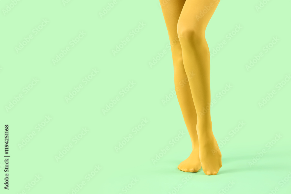 Legs of young woman in yellow tights on green background Legs of young woman in yellow tights on green background