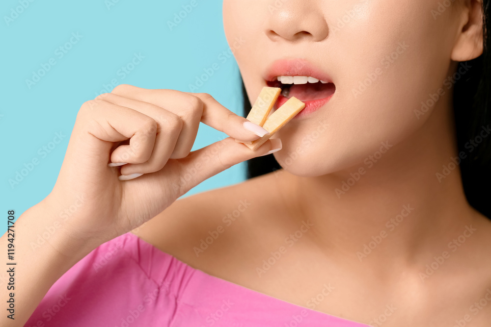 Pretty young Asian woman with open mouth holding chewing gums on blue background, closeup Pretty young Asian woman with open mouth holding chewing gums on blue background, closeup
