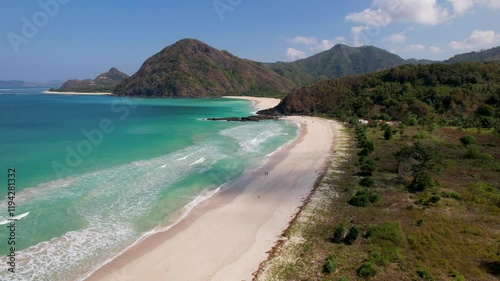 4K drone video of a couple walking along Selong Belanak Beach in Lombok, Indonesia. The long white sand beach has white waves rolling in from the clear blue ocean with mountains surrounding the beach photo