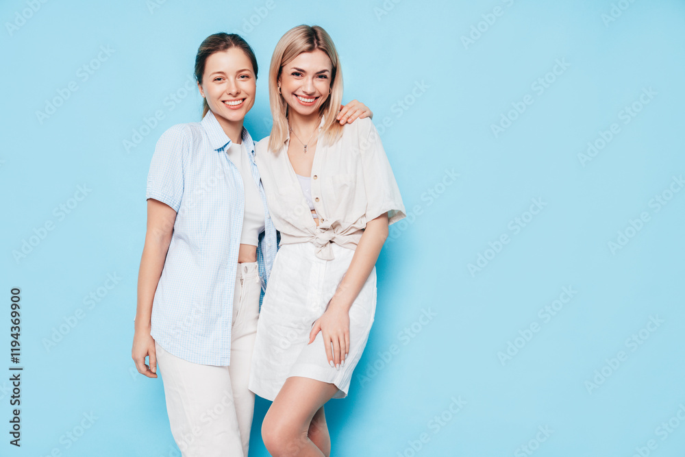 Two young beautiful smiling brunette hipster female in trendy summer clothes. Lovely women posing on blue background in studio. Positive models having fun. Cheerful and happy. isolated