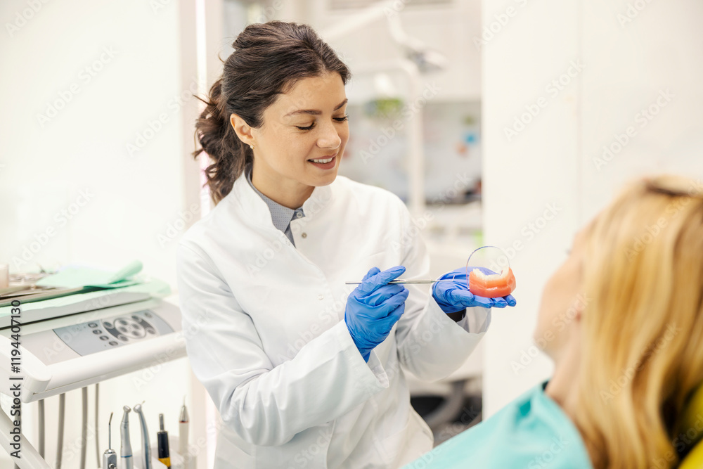 Dentist showing teeth model to a woman in chair at dentist office. Dentist showing teeth model to a woman in chair at dentist office.