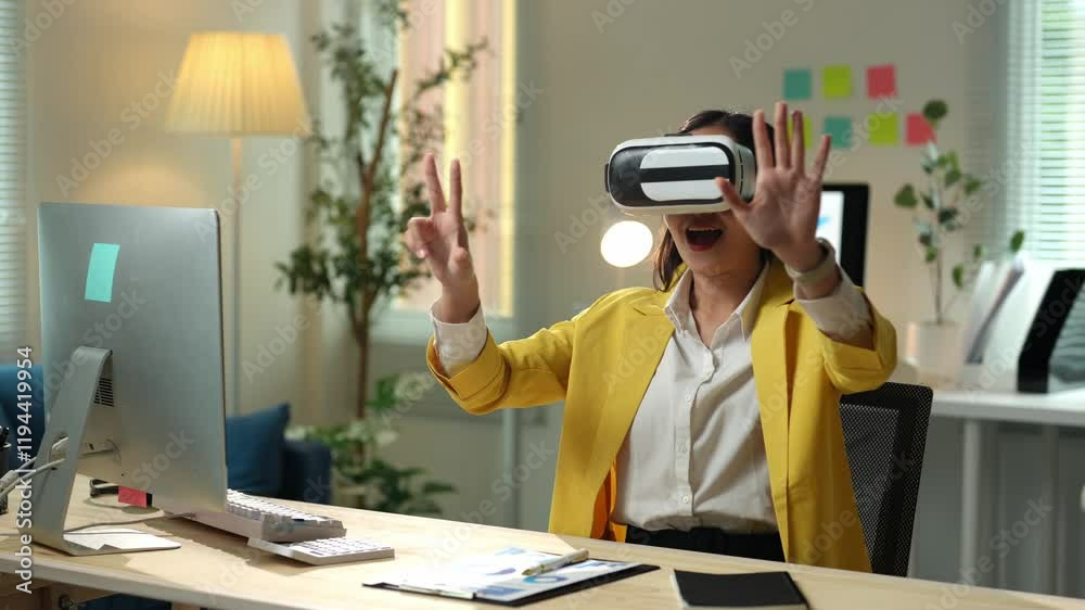 Young businesswoman wearing vr headset is sitting at desk in modern office and interacting with virtual reality, exploring immersive digital world