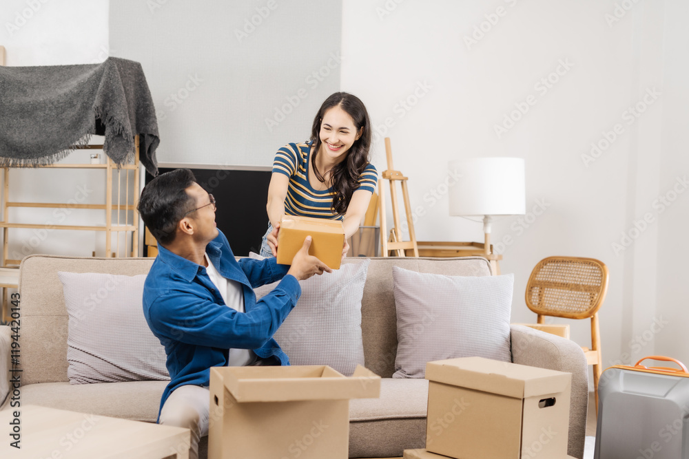 Young couple sitting on a sofa, helping each other pack, collecting clothes, putting items in boxes, feeling happy and excited while preparing to move into their new apartment Young couple sitting on a sofa, helping each other pack, collecting clothes, putting items in boxes, feeling happy and excited while preparing to move into their new apartment