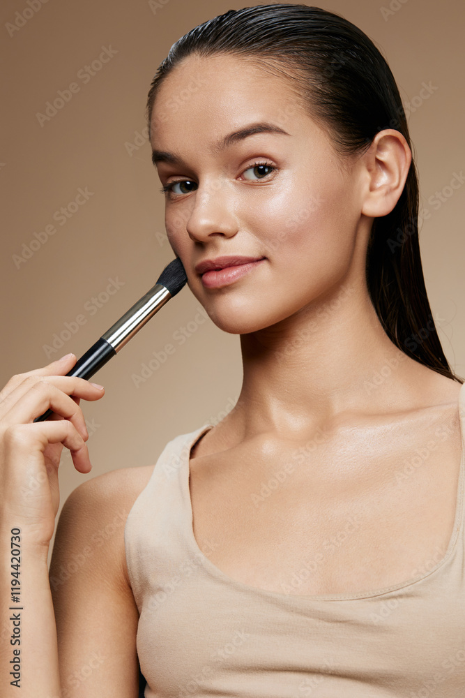 Young woman applying makeup with a brush, showcasing a natural beauty look, soft skin tone, and a neutral background for a fresh and elegant style Young woman applying makeup with a brush, showcasing a natural beauty look, soft skin tone, and a neutral background for a fresh and elegant style