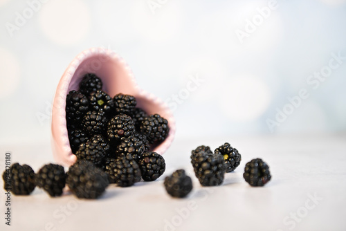 Blackberries spilling from a pink heart-shaped bowl on a light s photo