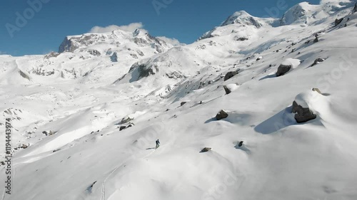 Aerial view of a skier on a ski tour next to Gorner glacier in Zermatt, Switzerland covered in snow on a sunny winter day with a view of the tallest peaks of the Swiss Alps including Monte Rosa.