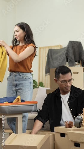 A happy young couple sits on a sofa, packing belongings into boxes, preparing to move to a new house, enjoying teamwork, organizing items, showing excitement, and embracing a fresh start