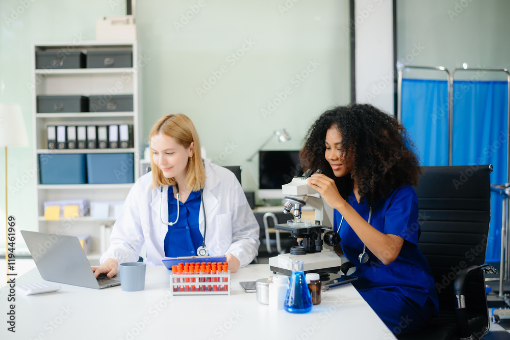 Fototapeta premium Focused Female doctor and African female nurse look at tablet and laptop screen discuss anamnesis together.