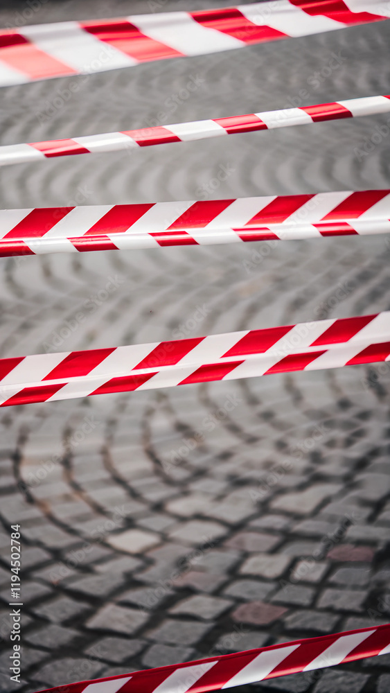 Tape barrier marking a danger zone on a stone-paved city sidewalk Tape barrier marking a danger zone on a stone-paved city sidewalk