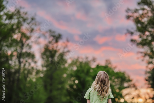 Child watching a vibrant pink and orange sunset in a forest clearing.