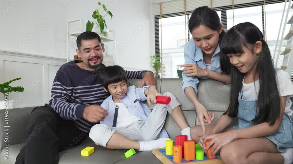 Family relaxing on sofa while kid drawing on floor. Happy Asian little girl enjoy playing a stacking blocks with her parent in living room in free time.