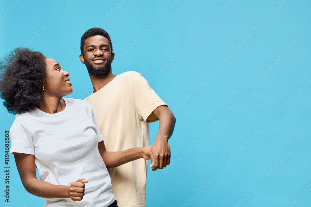 Obraz premium A joyful young couple dancing together against a vibrant blue background, showcasing happiness, connection, and fun in casual attire
