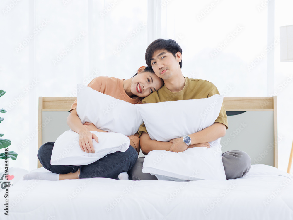 Portrait of young lovely sweet attractive asian happy couple love posing to camera smiling hugging pillow sitting on white bed in bedroom at home good time romantic together Valentine's day concept. Portrait of young lovely sweet attractive asian happy couple love posing to camera smiling hugging pillow sitting on white bed in bedroom at home good time romantic together Valentine's day concept.