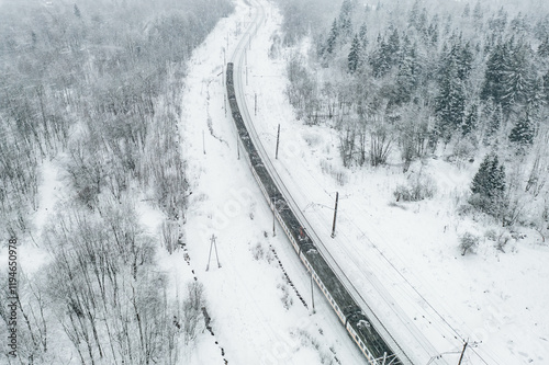 Aerial drone view of train in snow winter forest. Long commuter train moving to railway station.